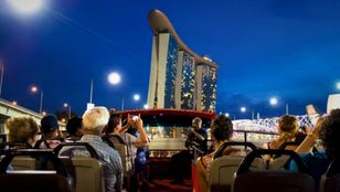 Excitement-filled night tour: Big Bus double-decker, a vibrant beacon, carries thrilled passengers through Singapore's illuminated streetscape.